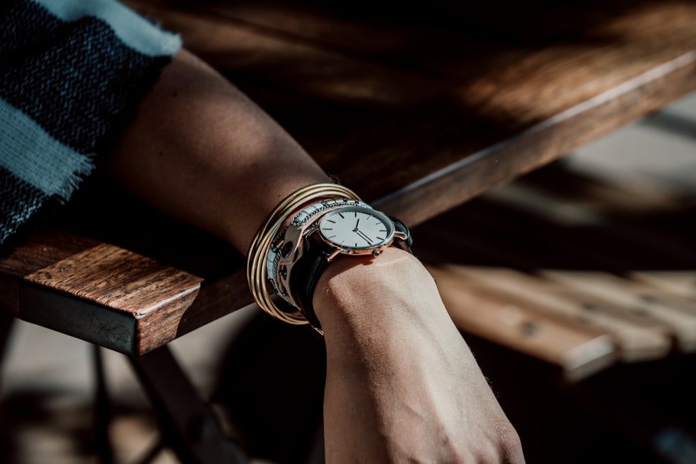 person wearing analog watch leaning on the table