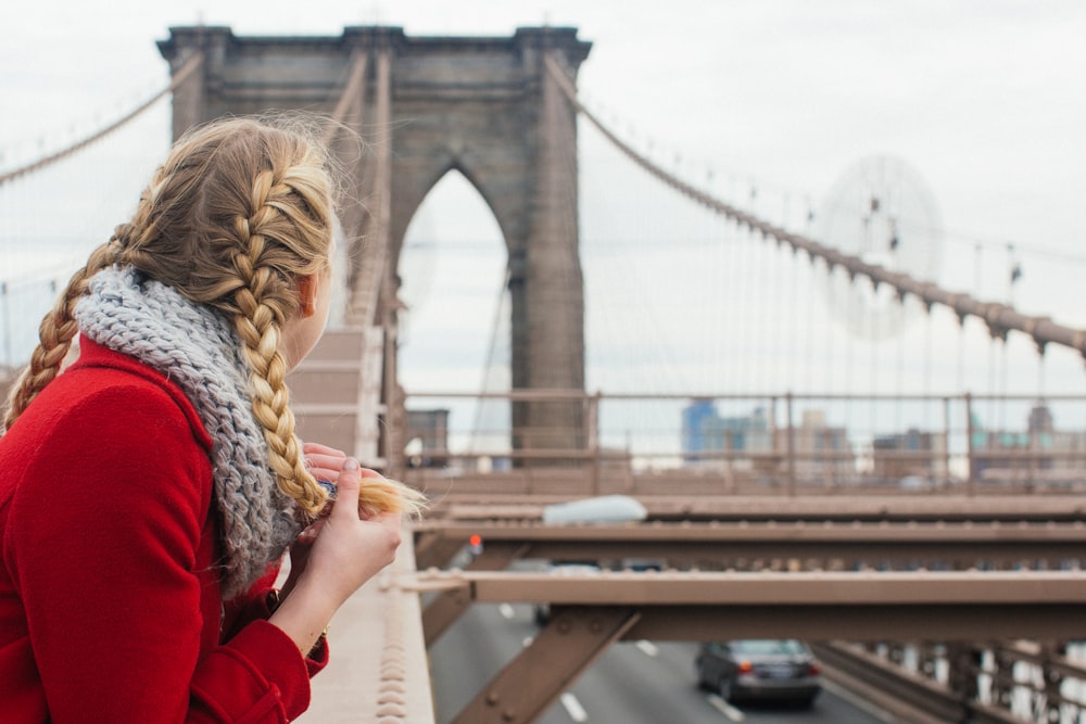 woman wearing red long-sleeved top leaning on metal beam while looking at bridge