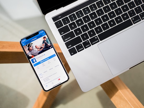 an image of an iphone with the facebook app open sitting on a glass table next to a macbook pro