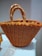 A large, intricately woven handbag featuring a crochet pattern in vibrant orange with yellow accents. The bag is placed on a white cloth, and the handles are wrapped with a textured, braided design.