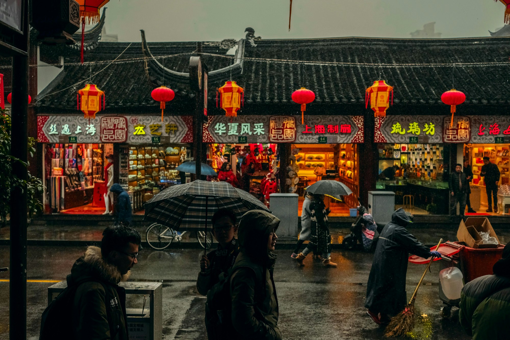 photograph of Chinese people walking through a historic alleyway in Shanghai, carrying umbrellas in the rain.