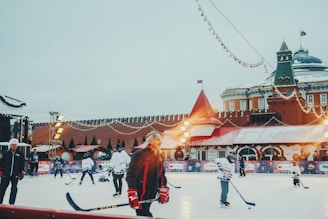 A lively outdoor arena with local players enjoying a sunny day on the ice rink surrounded by green fields.