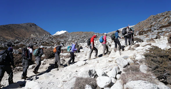 A rugged mountain trail with trekkers equipped in high-tech gear under a clear blue sky.