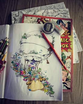 A collection of art supplies is laid out on a table, including colored pencils, a sharpener, and an eraser. There is a detailed sketch of an airship surrounded by whimsical creatures and patterns in vibrant colors on paper. Underneath are a couple of comic books, one prominently featuring a vintage-style cover with illustrated characters.