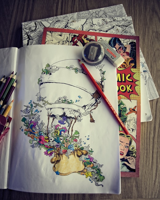 A collection of art supplies is laid out on a table, including colored pencils, a sharpener, and an eraser. There is a detailed sketch of an airship surrounded by whimsical creatures and patterns in vibrant colors on paper. Underneath are a couple of comic books, one prominently featuring a vintage-style cover with illustrated characters.