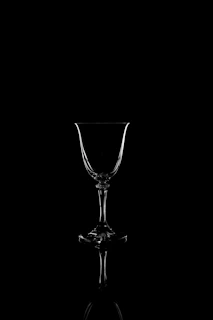 Close-up of a crystal wine glass catching muted gold light, set against a charcoal backdrop.