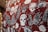 The image features a fabric with a bold, graphic pattern of white skulls wearing red 3D glasses, surrounded by various surfing-related elements like hands with surf-related text, surfboards, and text bubbles. The background is a deep red, creating a striking contrast with the white and black illustrations. The design includes phrases like 'CHILLAX,' 'RAD TO THE BONE,' and 'RIDE THIS WAY,' adding a playful, rebellious vibe.