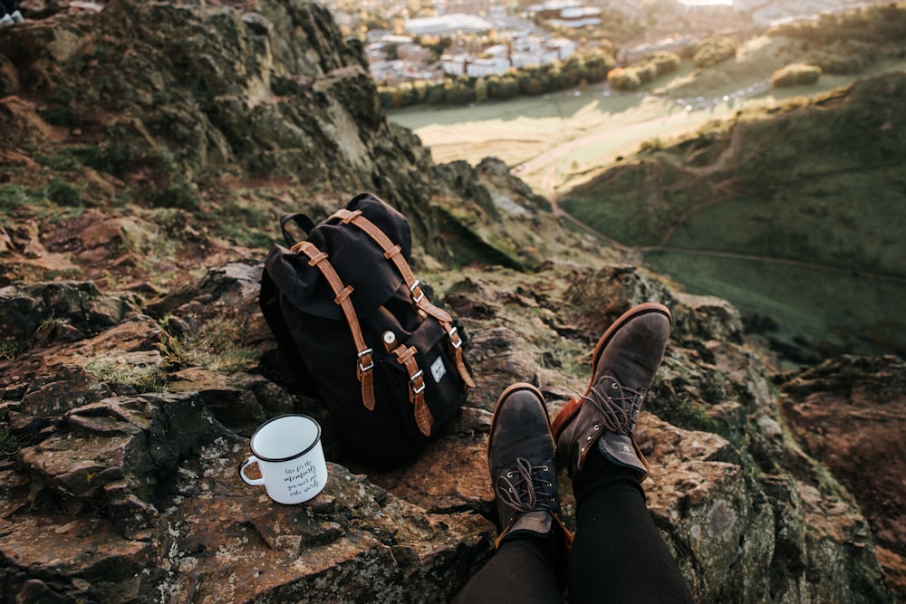 person wearing pair of brown boots sitting in front of black backpack