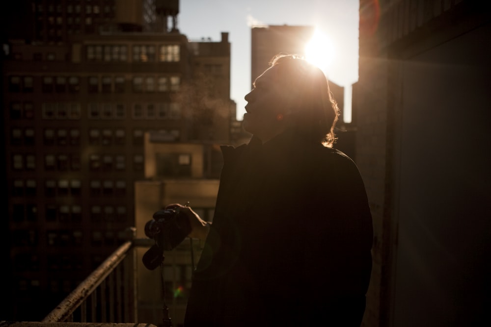 man in jacket holding camera on balcony during daytime