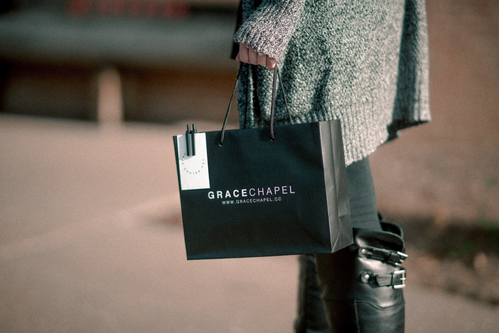 woman holding black paper tote bag