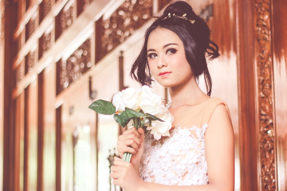 woman holding white rose standing near wooden wall