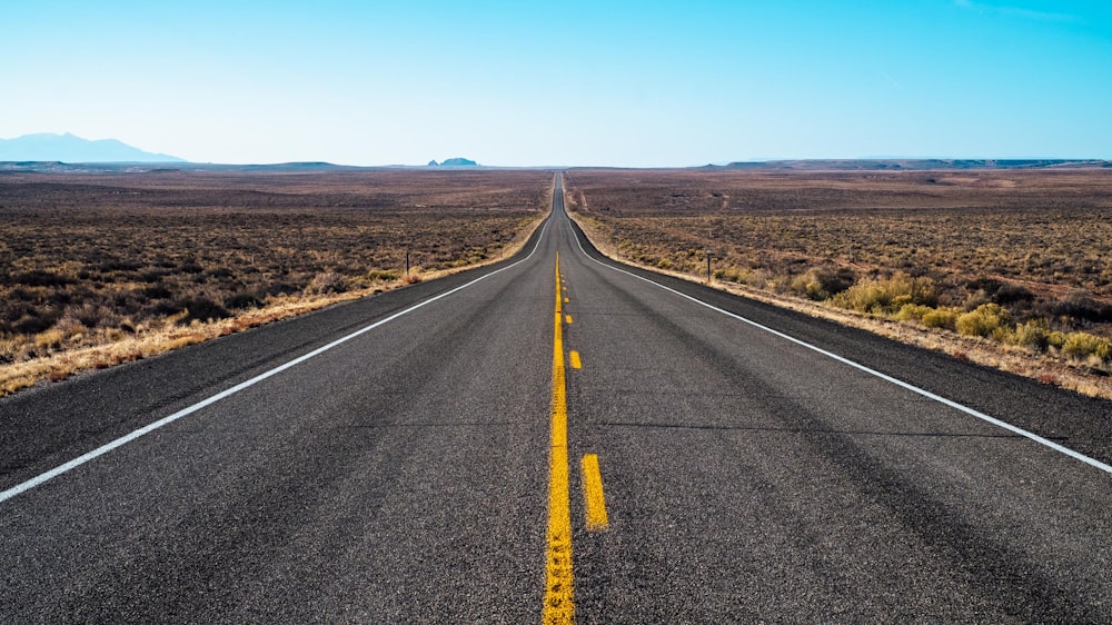 gray concrete road in middle of brown grass field