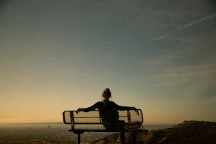 Person sitting quietly on a bench, gazing at the horizon with soft golden sunlight.