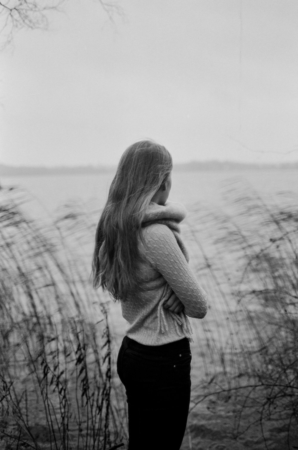 grayscale photo of woman standing near body of water