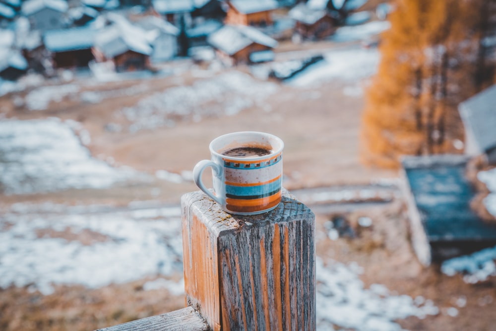 white, orange, and blue ceramic mug with brown liquid inside