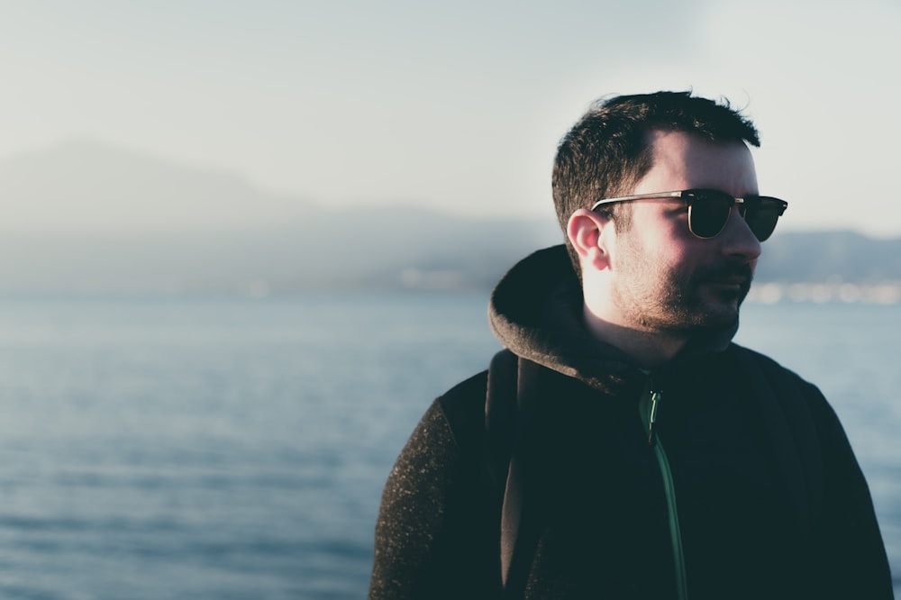 man wearing eyeglasses standing near body of water