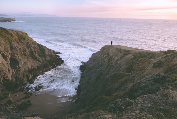 A serene scene of a person standing on a cliff overlooking a peaceful ocean at sunrise, symbolizing new beginnings.