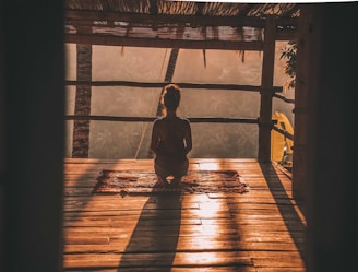 woman meditating on floor with overlooking view of trees