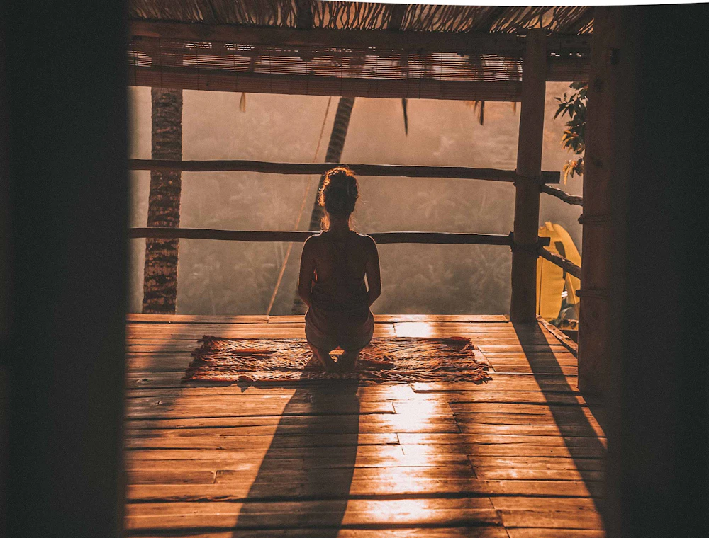 Woman meditating on the floor with an overlooking view of trees
