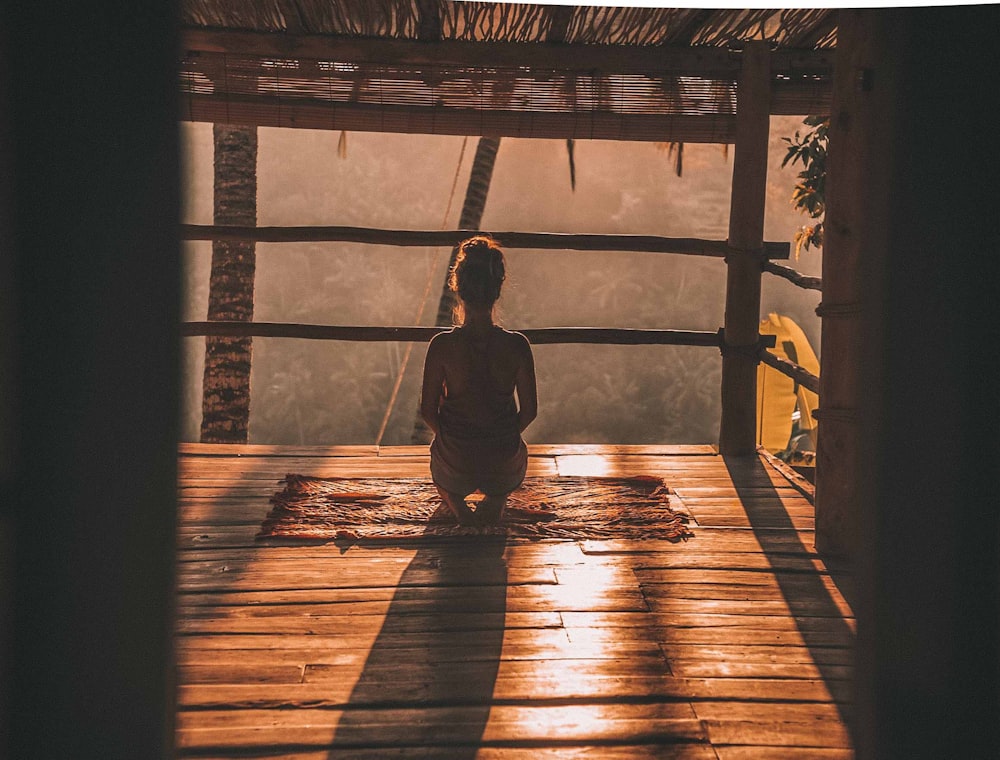 woman meditating on floor with overlooking view of trees