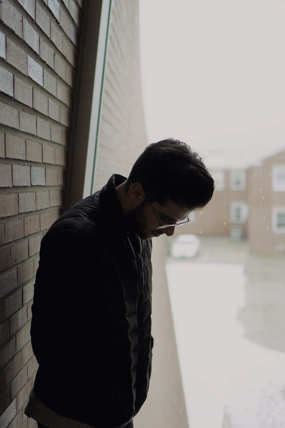 standing man wearing eyeglasses looking down near glass wall