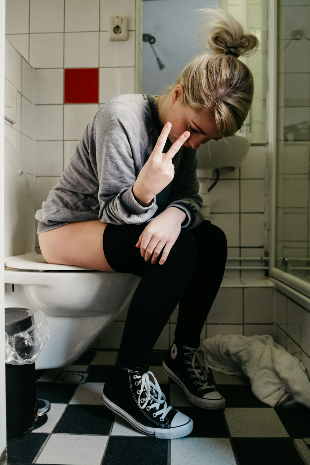 woman sitting on toilet bowl showing peace hand sign