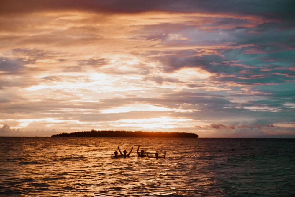 silhueta de pessoas nadando na praia durante a hora dourada
