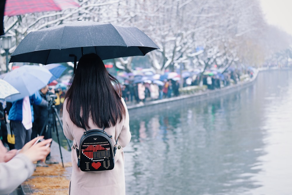 woman holding umbrella walking beside body of water