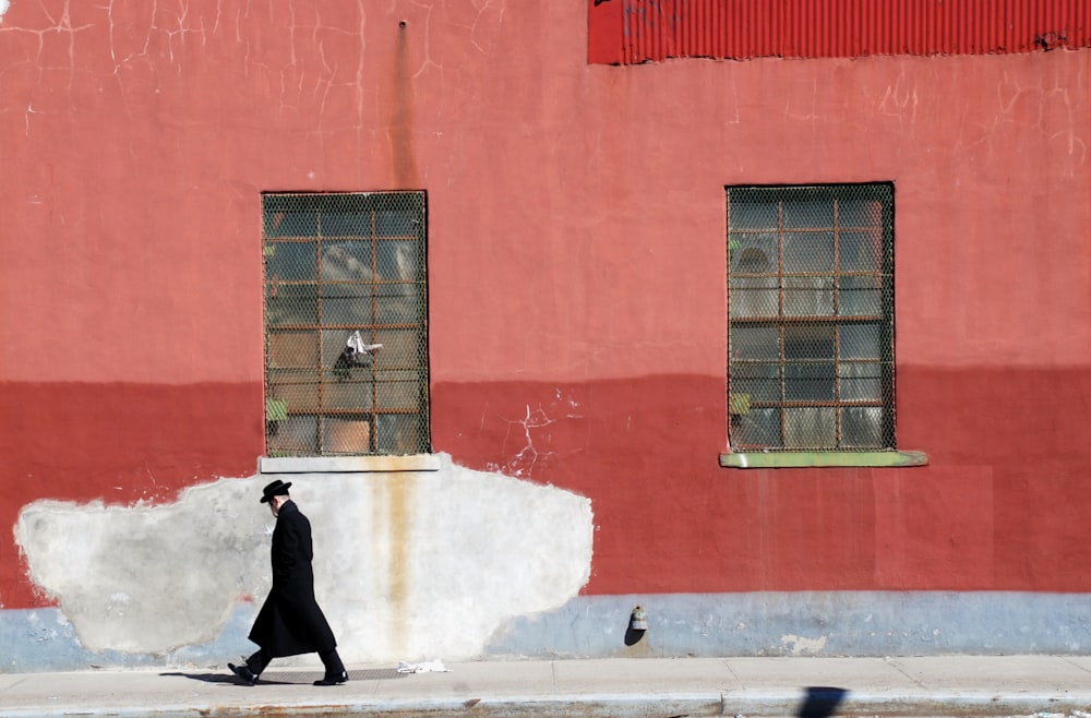 man walking beside red wall