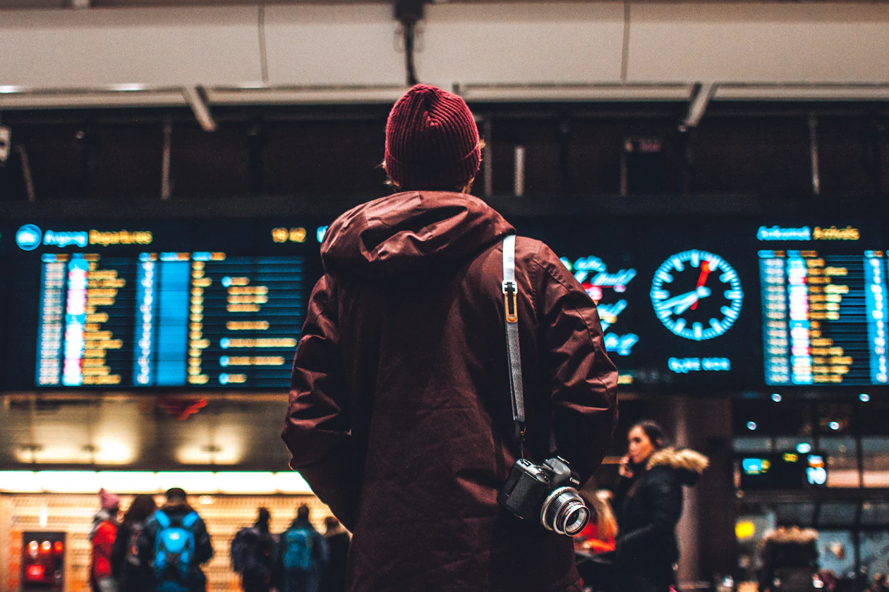 Traveler standing beneath a flight information board, checking departure times in a dimly lit transit terminal.