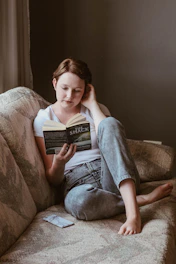 woman sitting on sofa while reading book inside room
