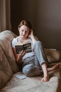woman sitting on sofa while reading book inside room