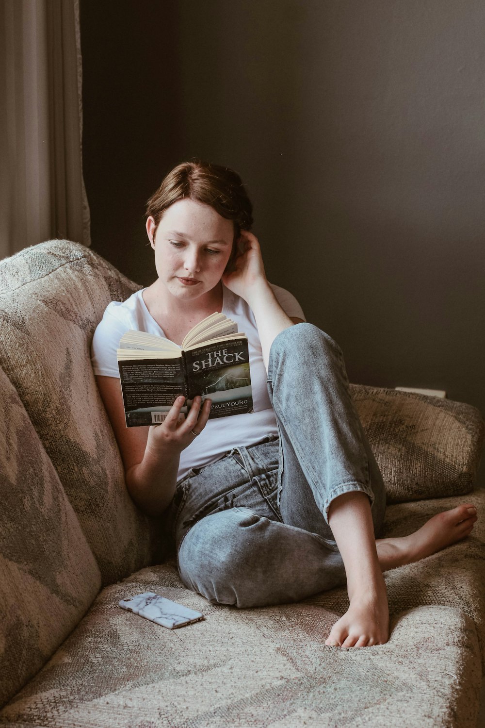Mujer sentada en el sofá mientras lee un libro dentro de la habitación