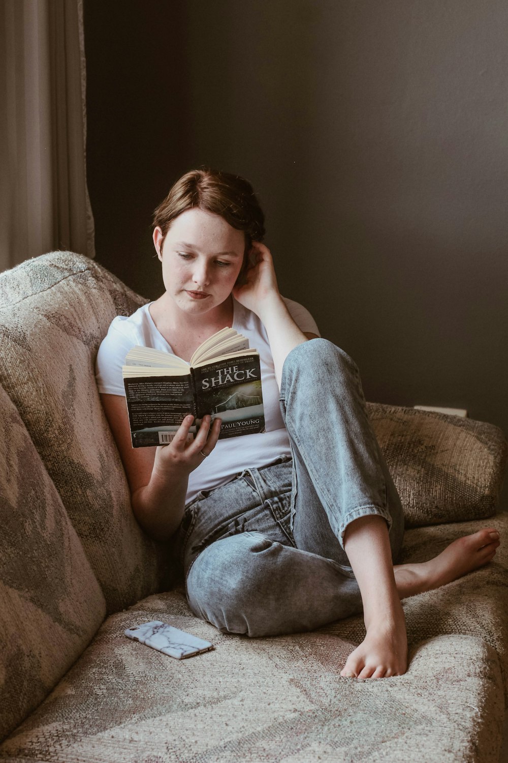 femme assise sur le canapé tout en lisant un livre à l’intérieur de la chambre