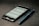 A smartphone displaying a web page is placed on a dark surface next to a blue pen. The phone screen shows a website with text and icons visible.