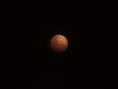 A celestial event captures the Earth's shadow covering the moon, giving it a reddish hue known as a blood moon, set against a black night sky.