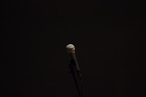 Black and white photo of a microphone stand with a coiled cable on a dimly lit stage