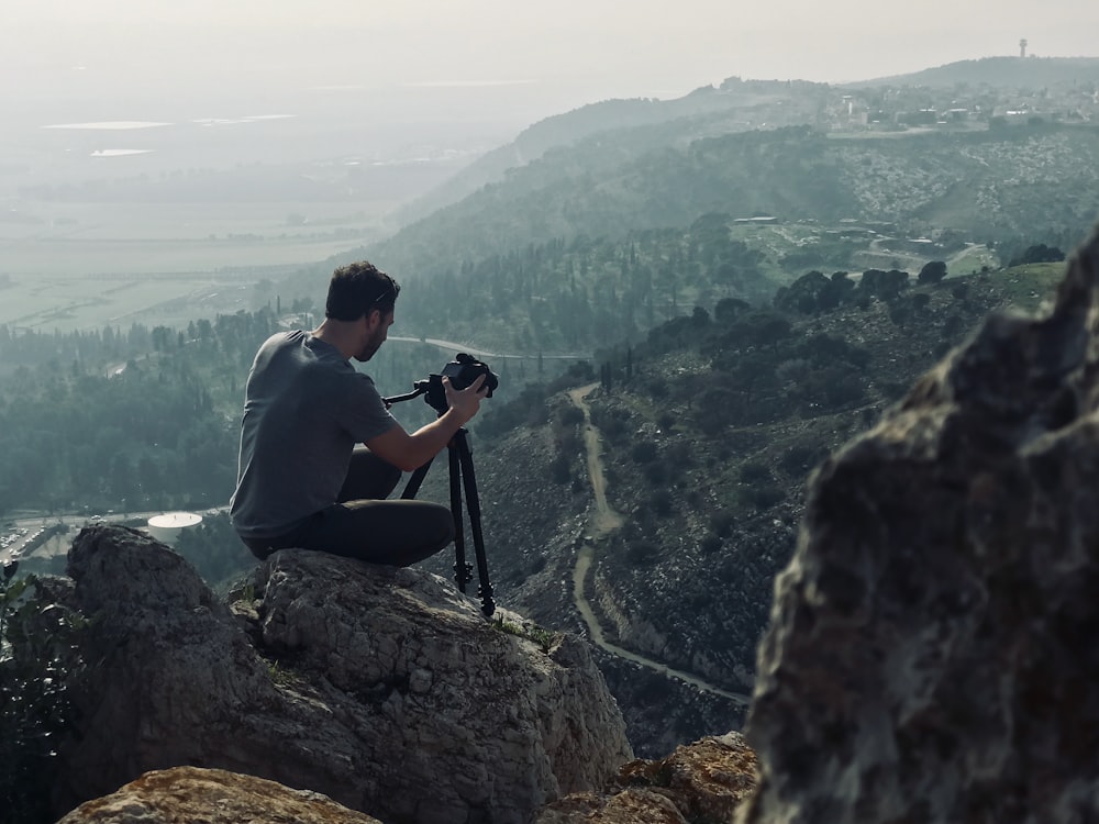 Mann sitzt mit Kamera auf einem Felsen