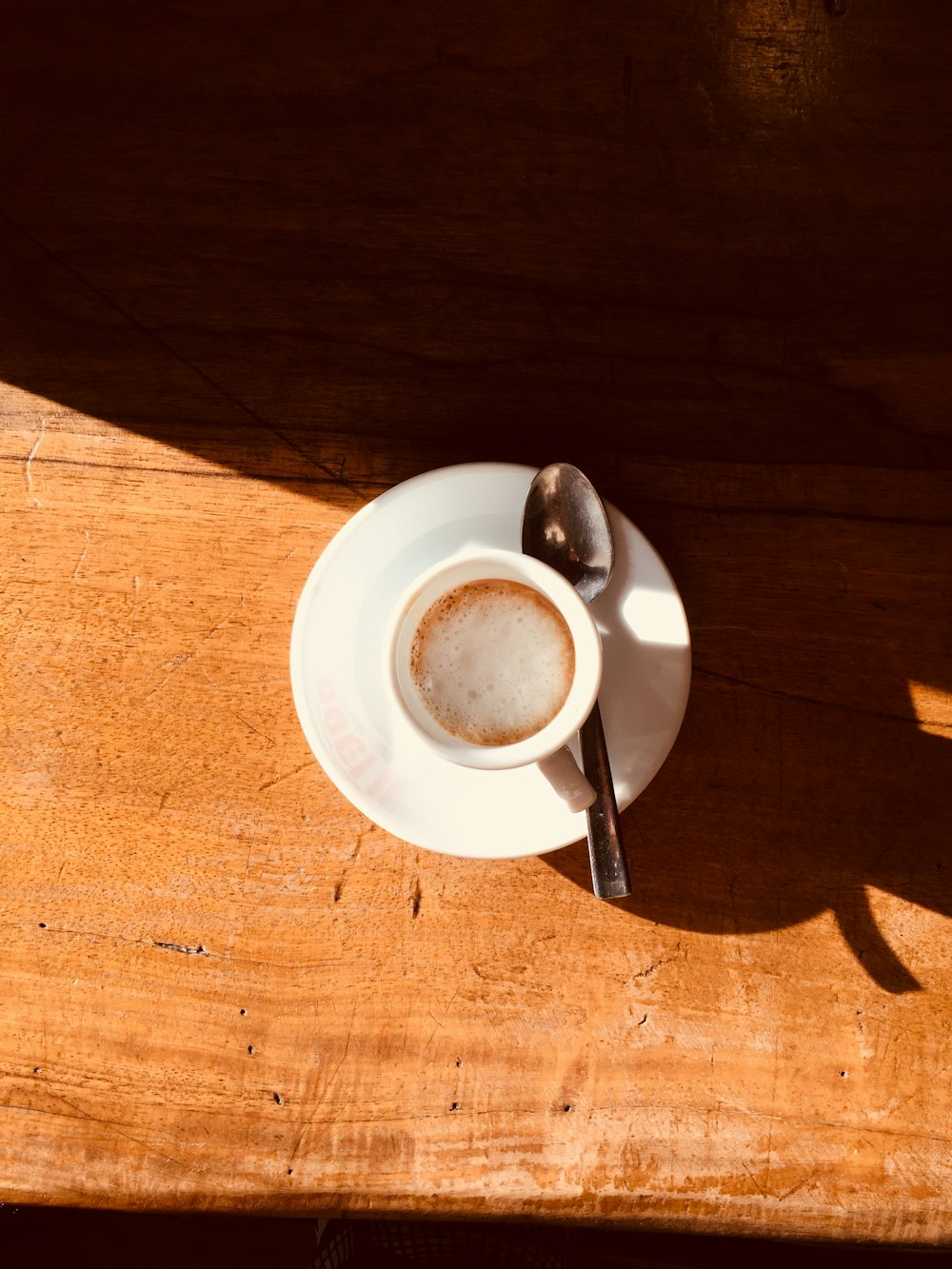 white cup and saucer and spoon on brown table