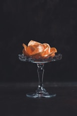 orange flower on glass footed vase against black background