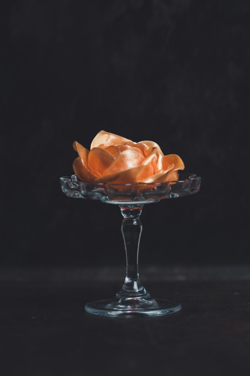 flor de naranja en jarrón con patas de vidrio sobre fondo negro