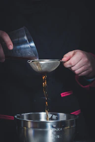 Close-up photo of a chef measuring ingredients beside stainless steel kitchen equipment in use.