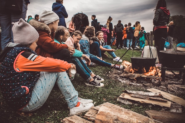 Children gathered around a campfire reenacting Stone Age life with handmade tools and costumes.