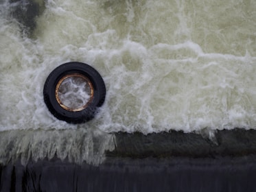 A black tire is partially submerged and surrounded by white, frothy water. The water appears to be moving rapidly, creating a swirling pattern around the tire.