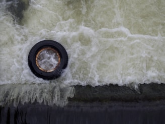 A black tire is partially submerged and surrounded by white, frothy water. The water appears to be moving rapidly, creating a swirling pattern around the tire.