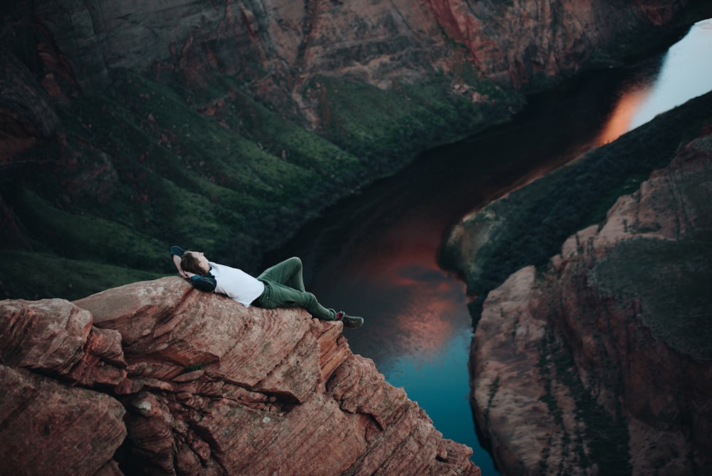 man lying on brown mountain near body of water