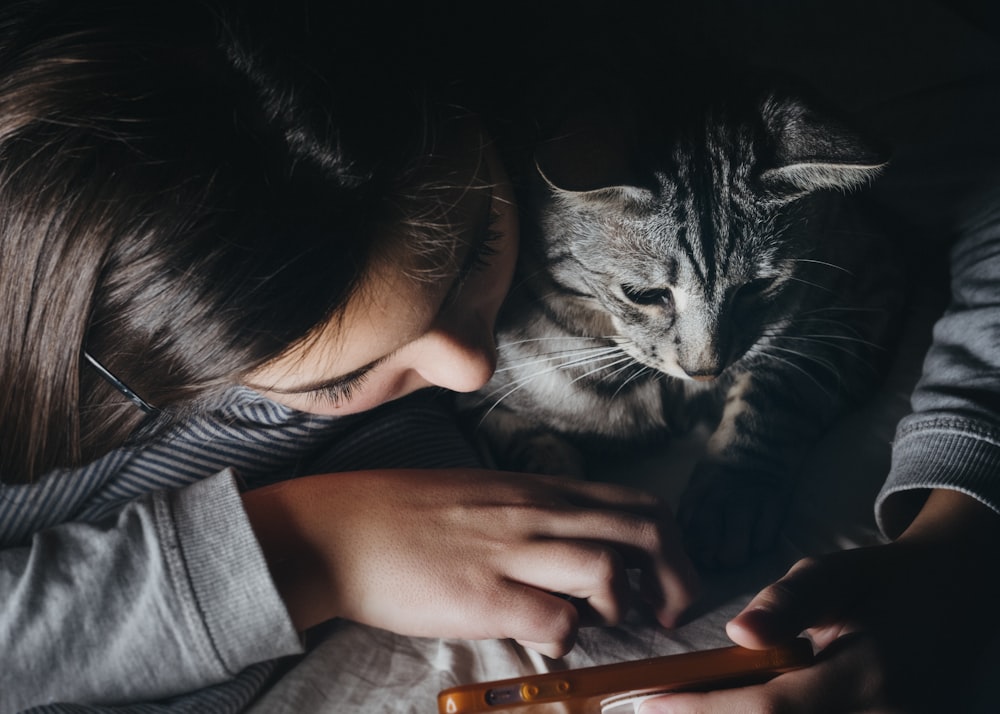 girl holding smartphone beside cat watching reclining to her shoulder