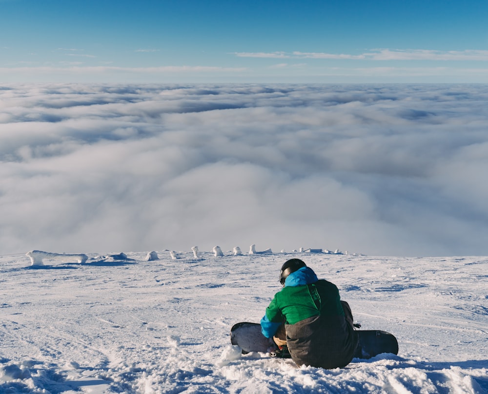 Person, die ein Snowboard hält, während sie auf Schnee sitzt