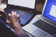 Hands typing on a Dell laptop with a blurred office environment in the background.