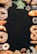 An assortment of baked goods, including bread, croissants, donuts, and pretzels, is arranged around the borders of a dark background. There are decorative elements such as green leaves and a small cup of coffee beans. The breads have different shapes, textures, and some are topped with seeds.